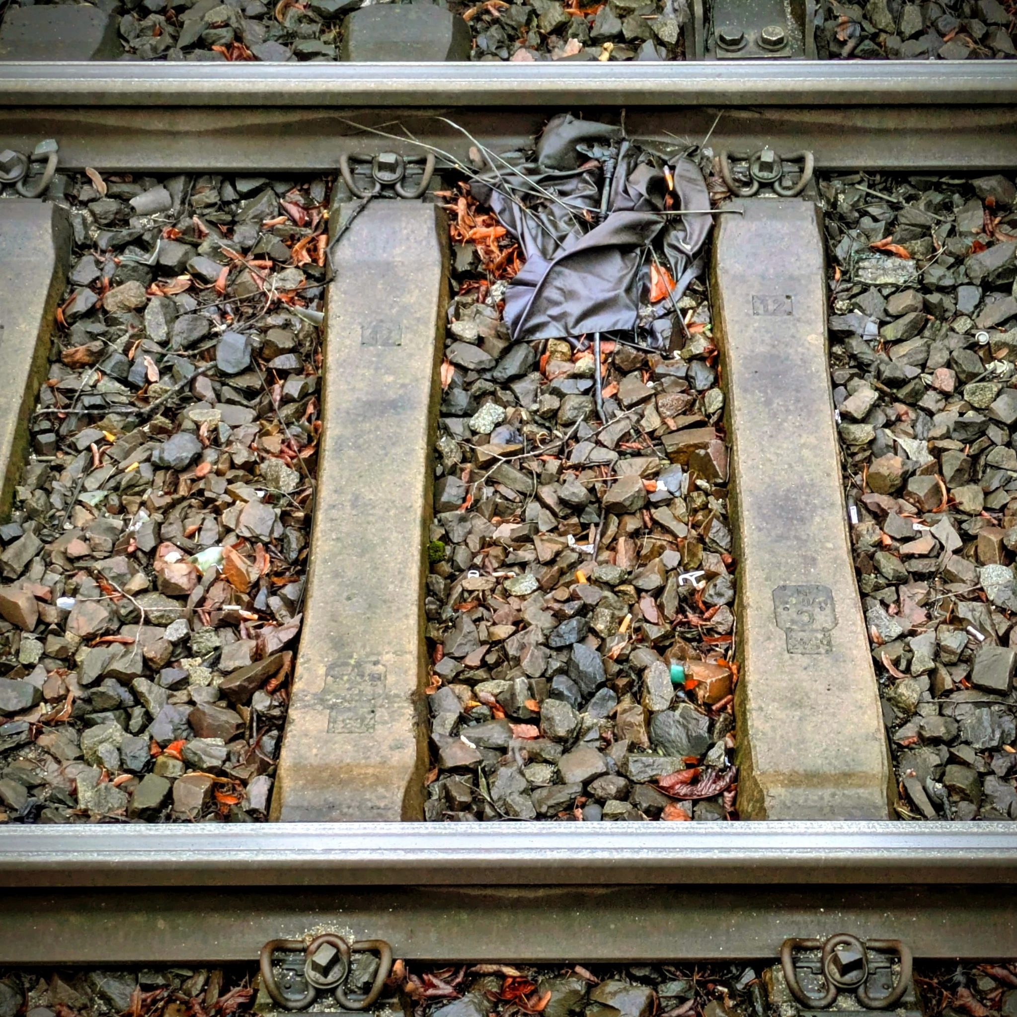 ein gleis im gleisbett vom bahnsteig gesehen, darin ein kaputter regenschirm