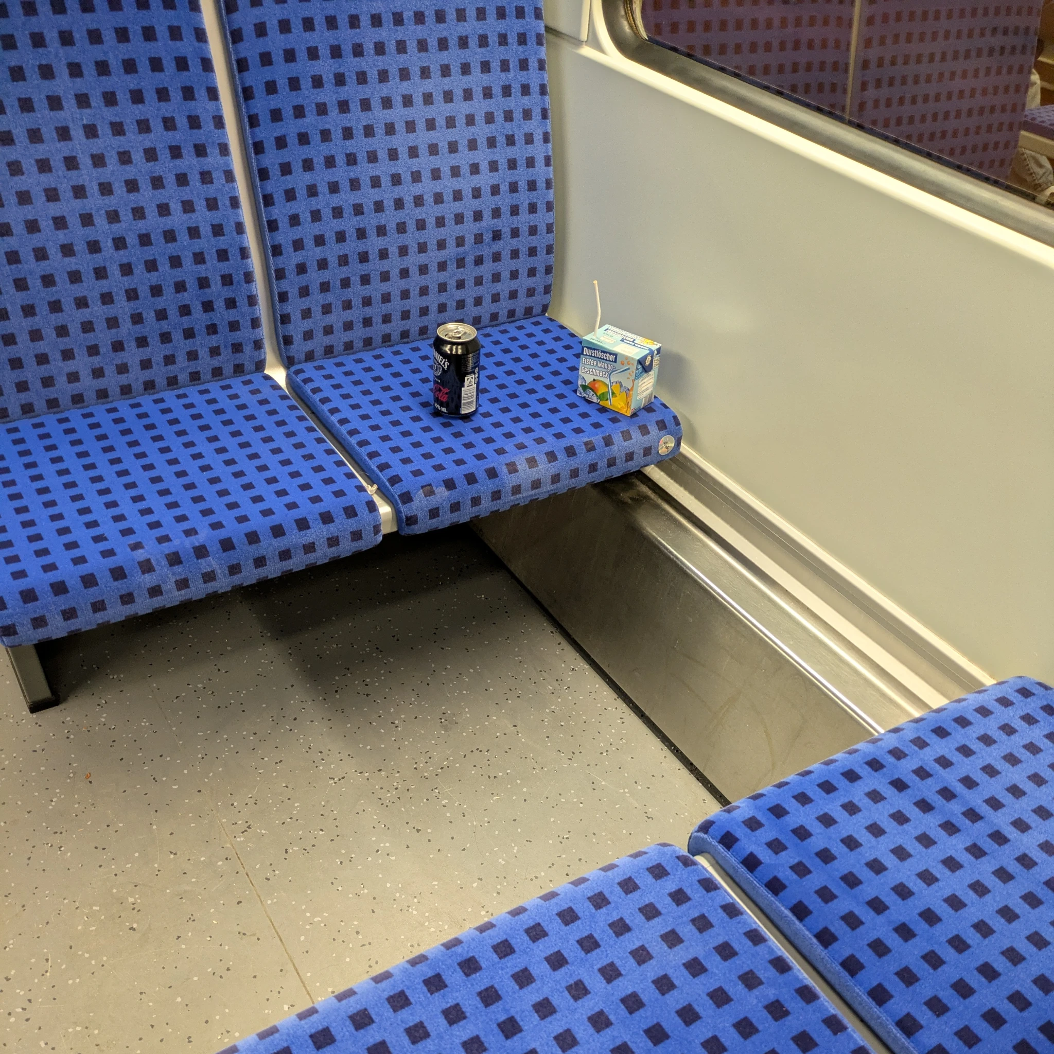 eine blau bezogene sitzgruppe in einer sbahn. keine fahrgäste am eine dose jackycola und ein eistee.