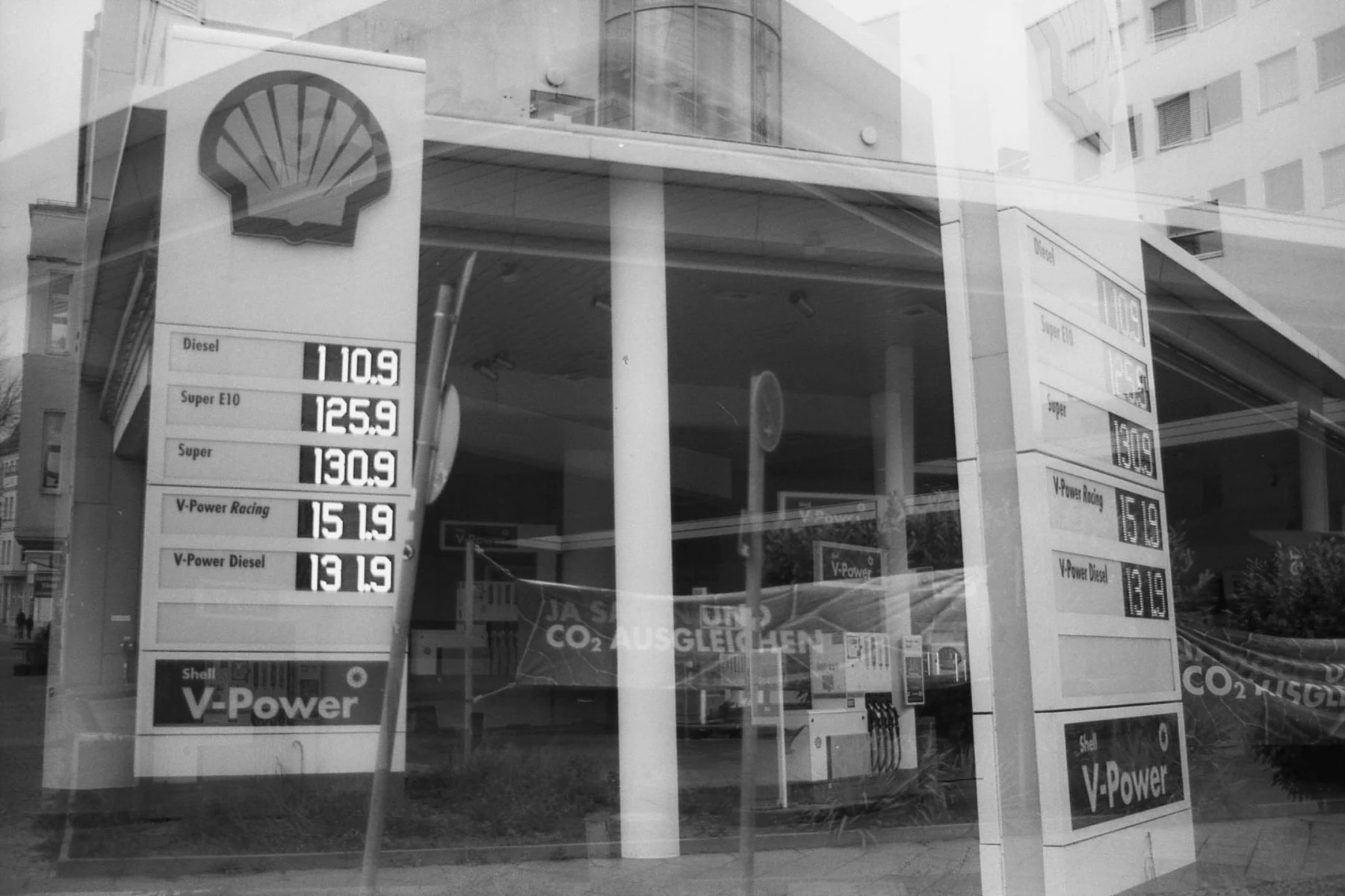 doppelt belichtetes schwarzweißbild. zu sehen ist eine tankestelle aus zwei blickwinkeln, prominent die preise, zB 125,9 € für einen Liter Super