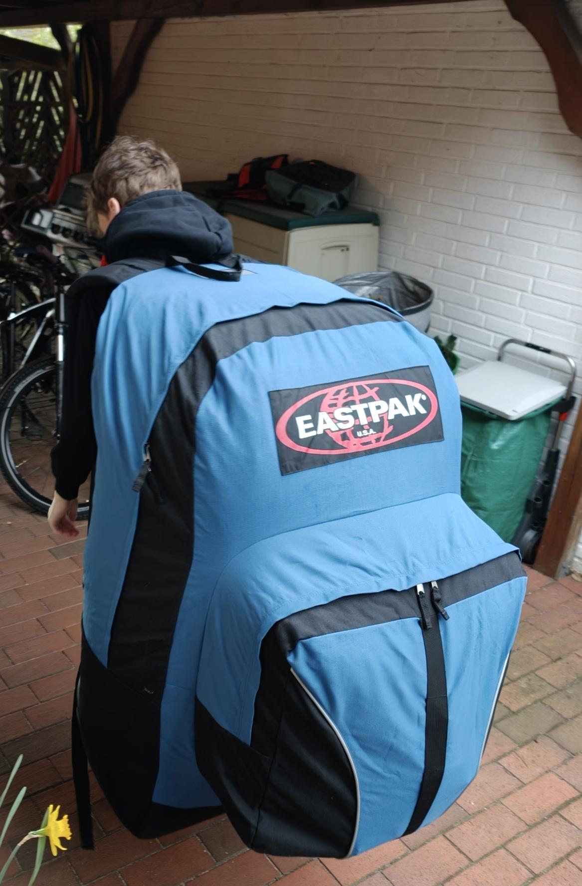 Bild vorm Haus im Innenhof aufgenommen. 
Teenager, ca. 1,75m groß mit gigantischem Eastpak-Rucksack in blau-schwarz der fast auf dem Boden schleift, geht Richtung Straße