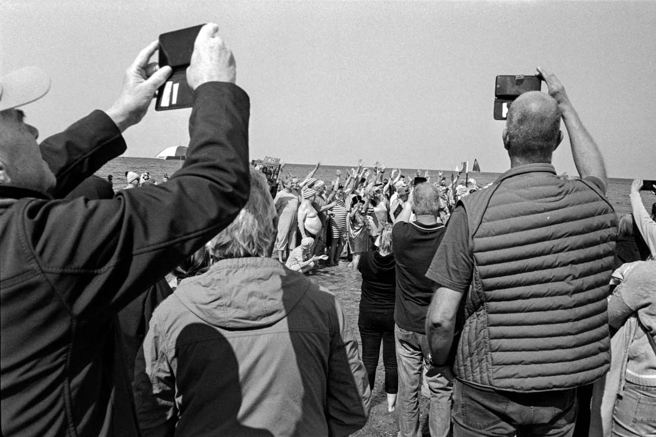 black and white scene of people in front of ocean with more people inside. some are filming some are just watching