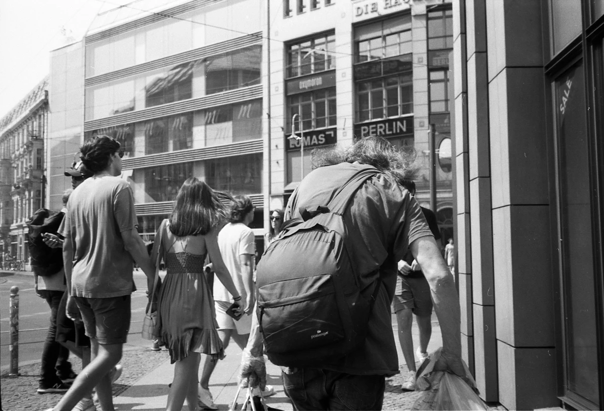 black and white photography of street scene in berlin mitte. several people seen from behind. some younger touristish looking couple. and one older with wild hair style and backback.