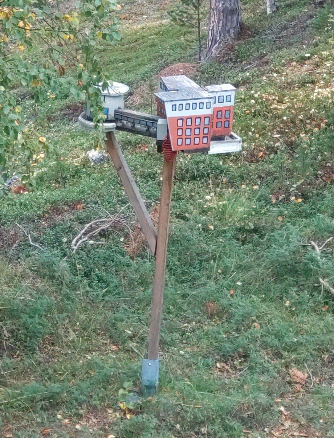 A bird feeder in a forest, designed to look like the building it sits outside of