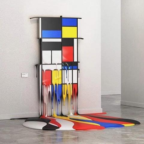 Een Mondriaan-achtig schilderij, rechthoeken in zwart, blauw, wit, geel en rood, dat in een grijze museumzaal een klein eindje van de muur hangt en waarvan de onderste helft smeltend en gesmolten is zodat er ook een kleurige plas op de grond ligt. 