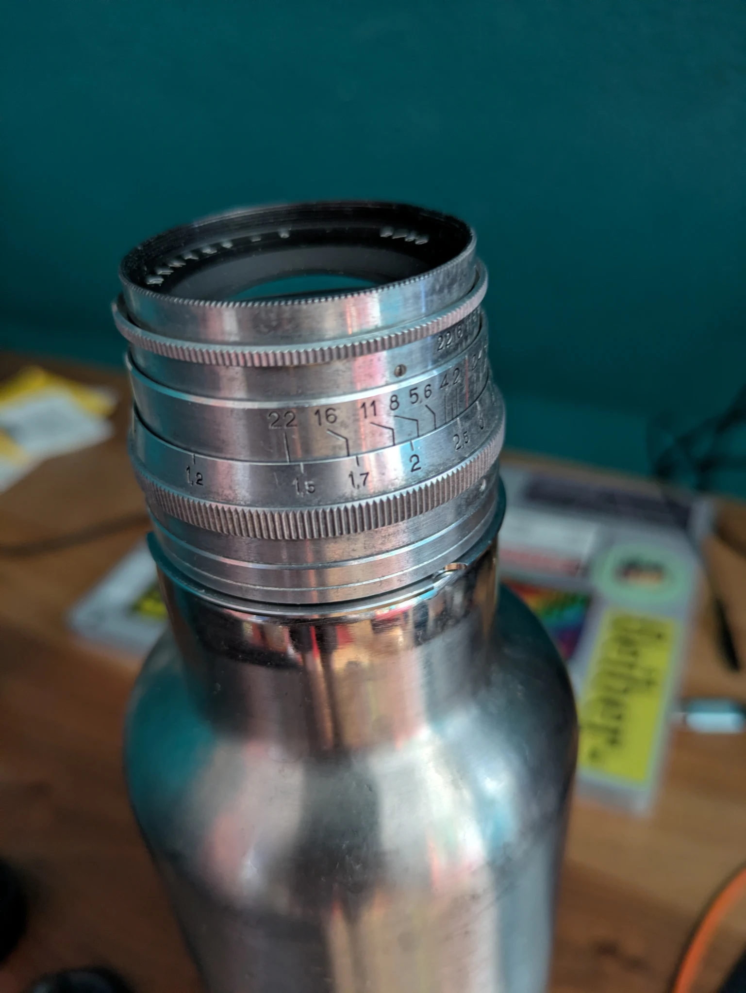 ein objektiv steckt auf einer metallenen trinkflasche, im hintergrund tisch und laptop
