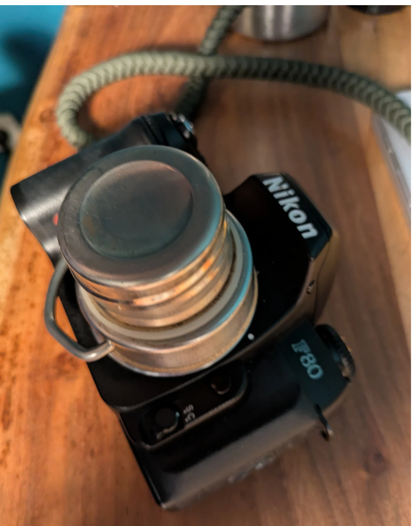 auf einer nikon slr liegt die metallene verschlusskappe einer trinkflasche als sei es das objektiv