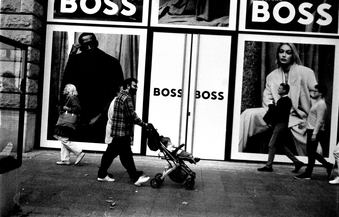 black and white picture with hard contrast. a store front with big letters saying BOSS. and peaple walking by.