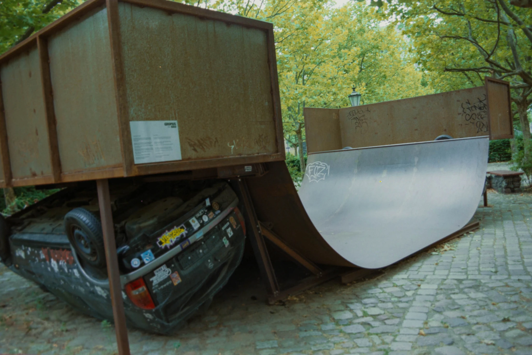 eine hölzerne halfpipe für skater, drunter liegt ein älteres auto auf dem dach