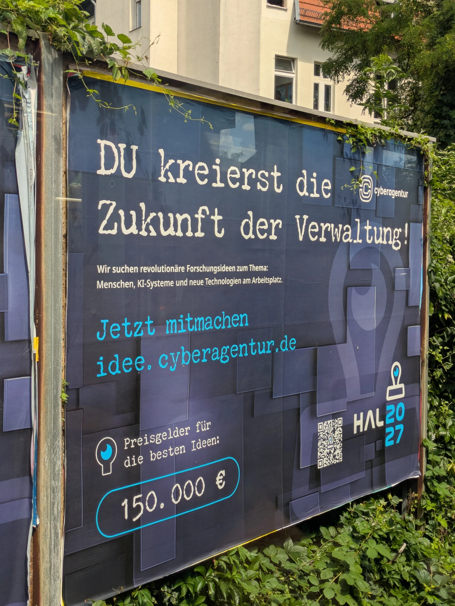 ein plakat an der sbahntrasse, von grün umwuchert, im Hintergrund häuser. auf dem plakat 

DU kreierst die Zukunft der Verwaltung und eine url idee.cyberagentur.de