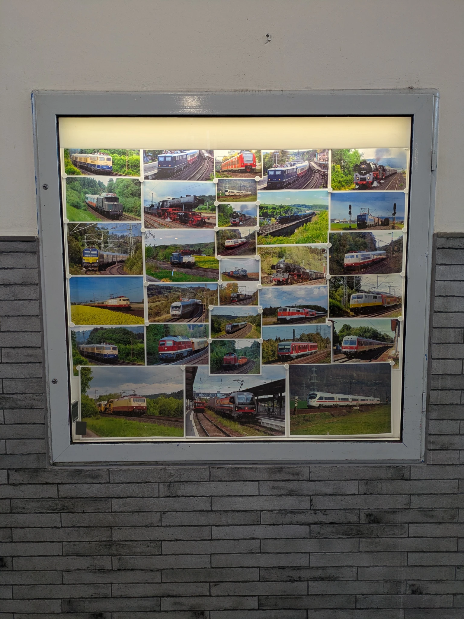 ein Schaukasten in einer wand, beleuchtet. darin ganz viele bilder von eisenbahnen