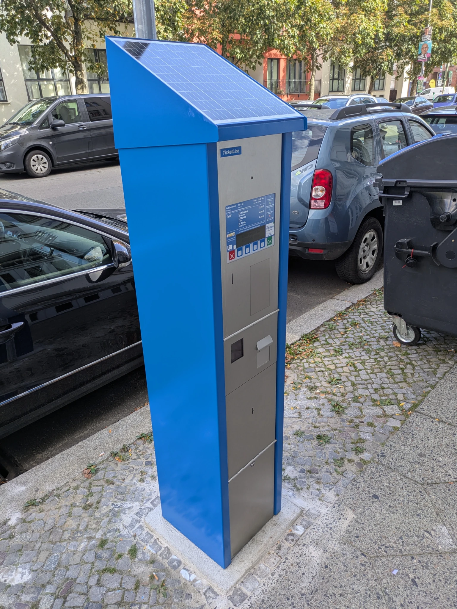 auf dem gehweg neben geparkten autos ein strahlend blauer parkscheinautomat