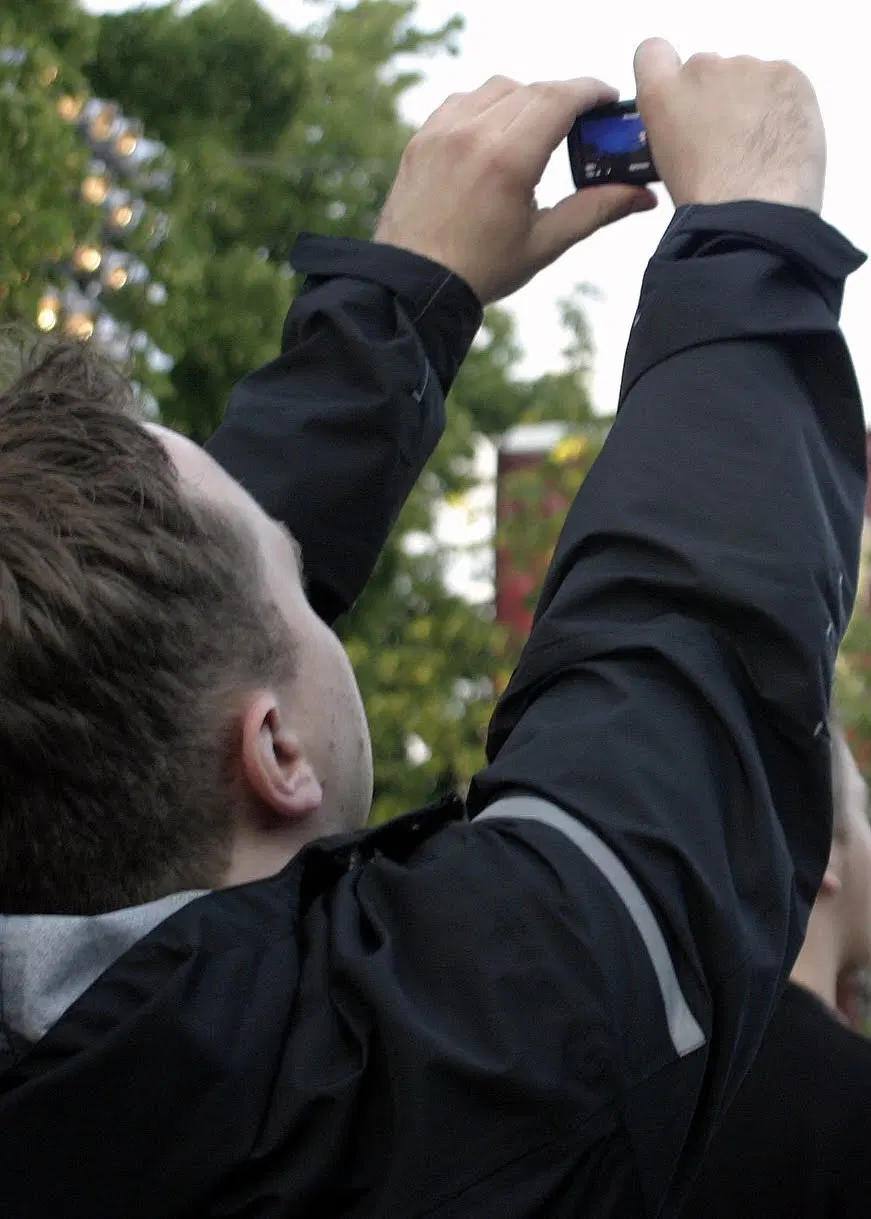 eine person hält eine art kamera oder handy in die höhe und film damit, wir betrachten sie von hinten