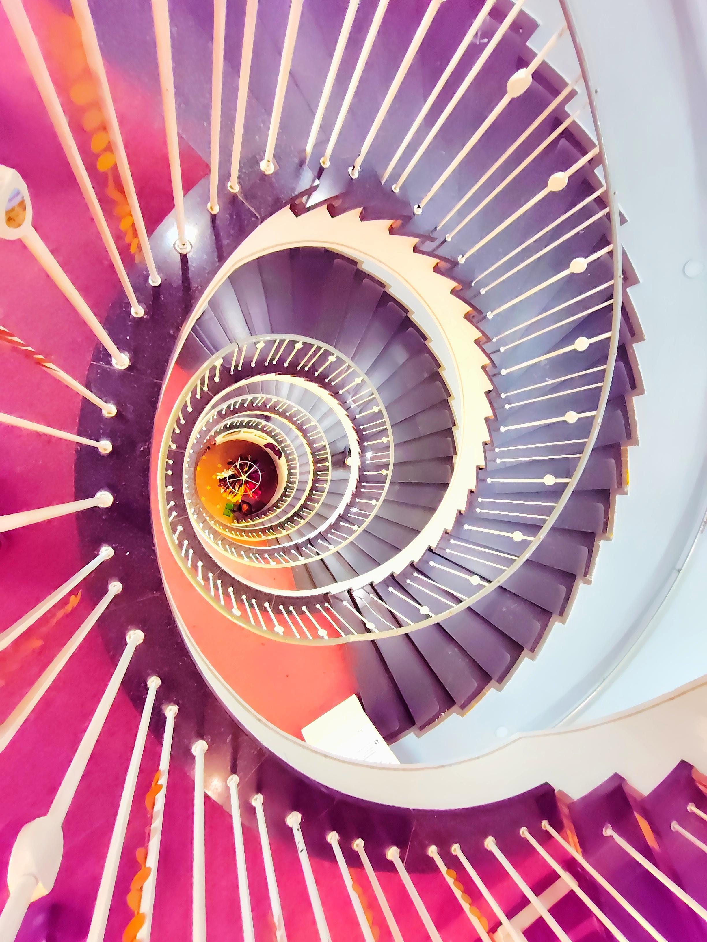 Gewendelte Treppe, Blick von oben durch vier Etagen. Die Farben des Bildes sind unnatürlich pink und lila. 