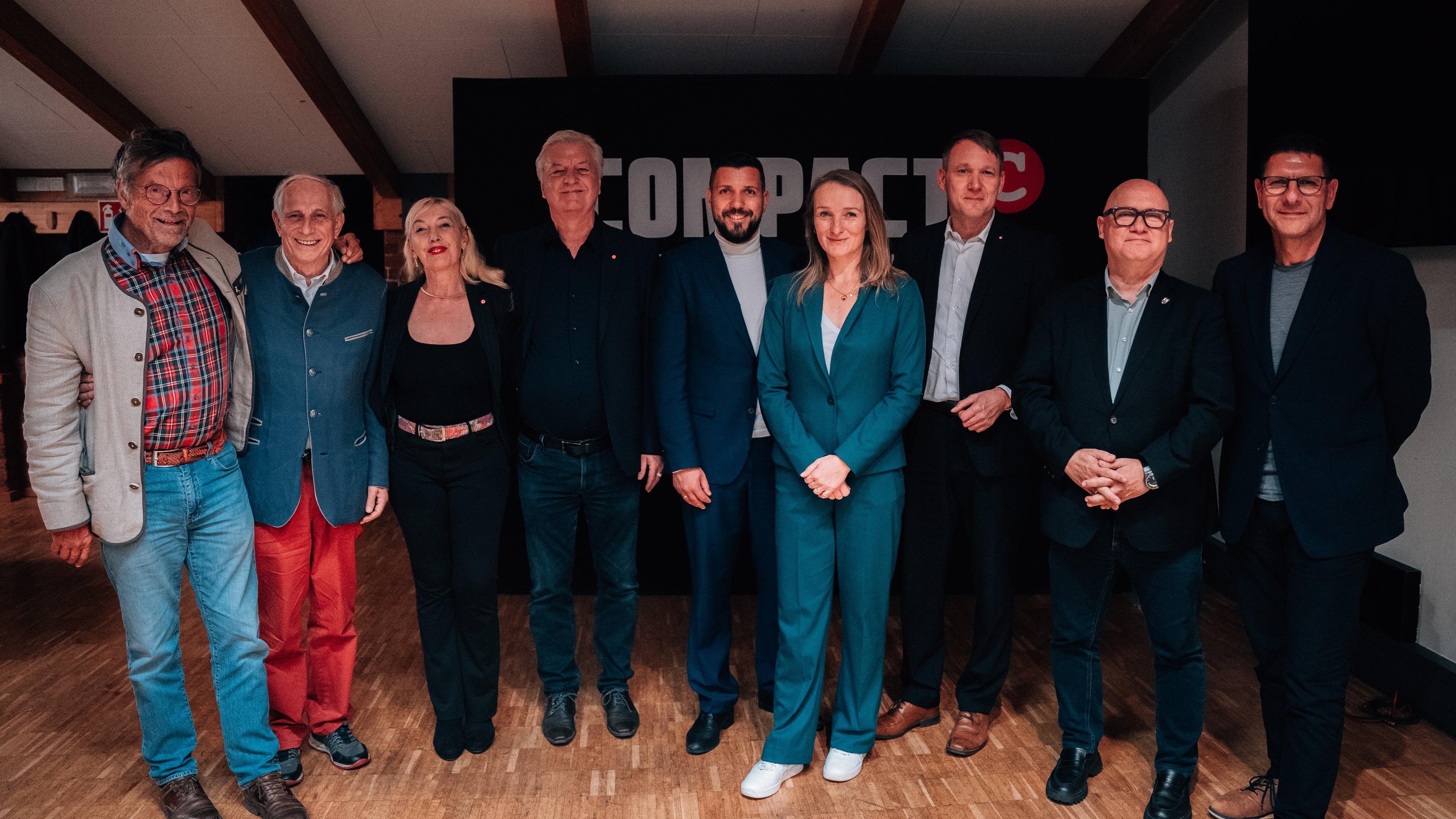 Gruppenbild von der Eröffnungsfeier des Compact-Studios. 9 Personen posieren nebeneinander vor einem großen Compact-Banner, von links nach rechts: Dieter Dehm, Alexander von Bismarck, Stephanie Elsässer, Jürgen Elsässer, Tobias Rausch (AfD), Claudia Wittig (BSW), Andre Poggenburg, Oliver Kirchner (AfD), Thomas Schulze (BSW).